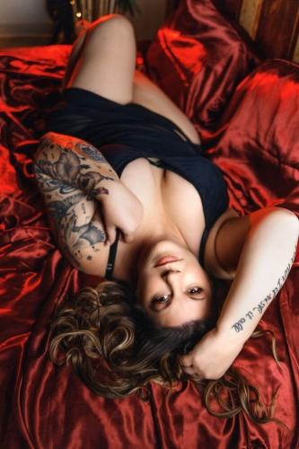 Boudoir picture of woman in black lingerie laying on her back on a red satin sheet.